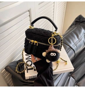 Close-up of black tweed chain bag with gold zippers and a fuzzy monster charm