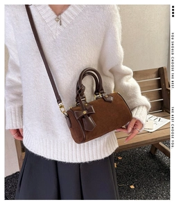 Detailed close-up of dark brown suede cylinder bag with bow charm and golden hardware