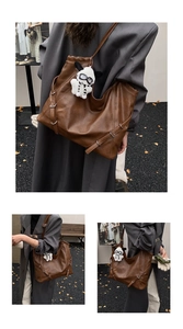 Detail of a brown leather tote bag featuring a cute plush panda charm and side buckle