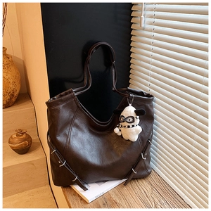 Detail of dark brown tote bag featuring side metal buckles and a cute plush lamb charm