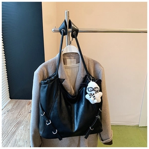 Detail view of large black tote bag with side metal buckles and white plush puppy charm