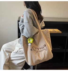 Detalle del bolso tote de pana beige con bordado de perro y colgante de flor amarilla