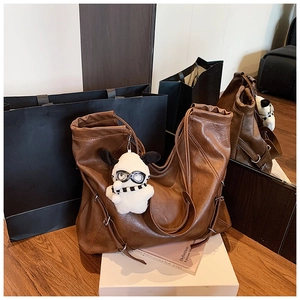 Detail view of brown soft leather tote bag featuring drawstring metal rings and plush dog charm