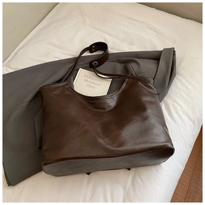 Detail of vintage brown leather tote bag with silver eyelets on a gray suit background