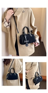 Detail of black suede Boston bag with golden hardware and cute bow charm accessory