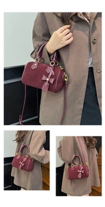 Detail of burgundy Boston bag showing suede texture, metal zipper and leather bow charm