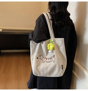 Detalle del bolso tote de pana con bordado de perro salchicha y colgante de flor de peluche