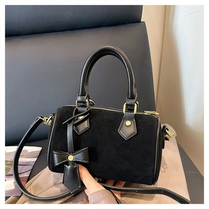 Close-up of black velvet Boston bag with gold metal buckles and bow charm detail