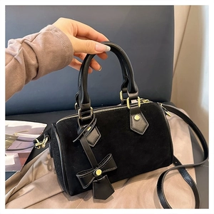 Detail of black velvet pillow bag with leather handles and gold hardware shown by hand