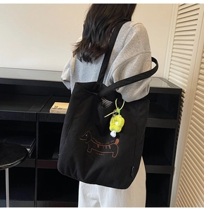 Detalle de bolso tote de pana negra con bordado de perrito y un colgante de flor verde