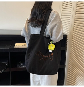 Detalle del bolso tote de pana negra con bordado de perro y un colgante de flor amarilla