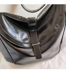 Close-up of glossy black leather handbag with metallic silver buckle and fine stitching