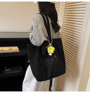 Detalle del bolso tote de pana negra con bordado de perro y un colgante de flor amarilla