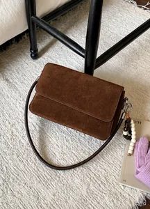 Detail of dark brown suede shoulder bag with wood bead charm on a soft plush rug