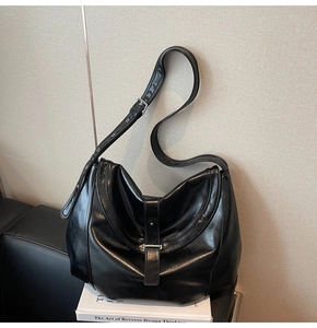 Detailed shot of a black glossy leather saddle bag with silver hardware on a sofa