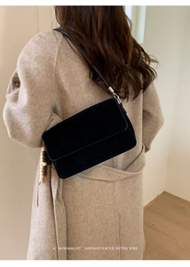 Detail of minimalist black suede shoulder bag with retro wooden bead charm on model