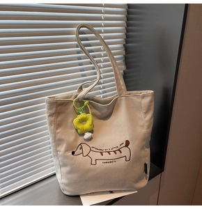 Detalle del bolso tote de pana con un bordado de perro salchicha y colgante de flor amarilla