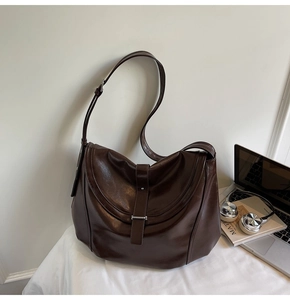 Detail of a dark brown vintage saddle bag shown in an office setting with a laptop