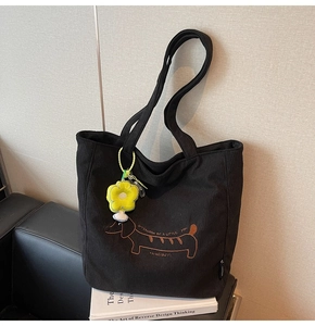 Detalle de bolso tote de pana negra con bordado de perro salchicha y colgante de flor amarilla
