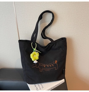 Detalle del bolso tote de pana negra con bordado de perro y colgante de flor amarillo