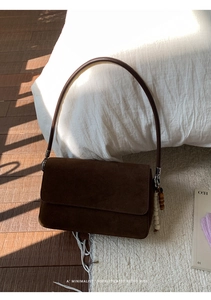 Detail of brown suede shoulder bag featuring a premium wooden bead charm and flip cover