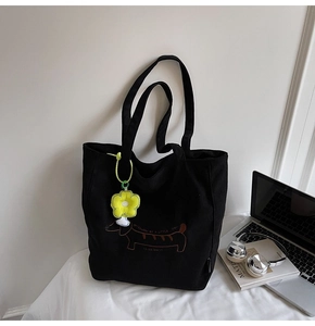 Detalle de teckel bordado en bolso de pana negra con colgante de flor amarilla