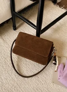 Detailed close-up of dark brown suede shoulder bag with decorative bead chain on rug