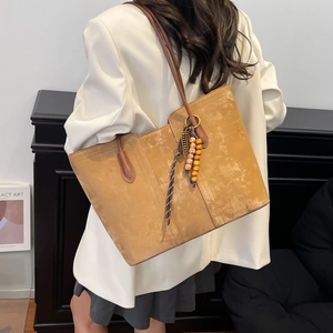 Large brown tote bag with woven charm and colorful beads shown on model in a modern room