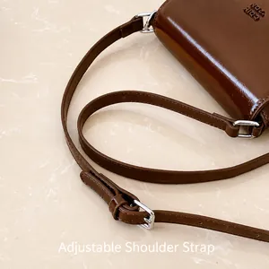 Detalle de la correa ajustable y hebilla de metal plateado en un bolso de hombro marrón oscuro