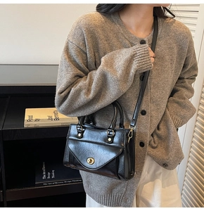 Detail van een vintage zwarte leren crossbodytas met een retro ronde metalen draaisluiting