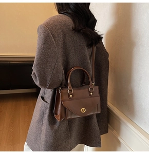 Detailopname van een vintage bruine leren handtas met gouden draaislot gedragen door model