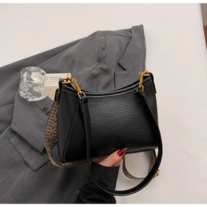Detalle de bolso tote de cuero mate negro con hebilla dorada y correa tejida