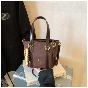 Detail of suede handbag with gold logo and colorful beaded charm on a silver suitcase