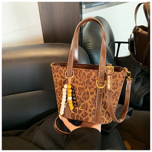 Detail view of leopard print tote bag with brown glossy handles and gold letter charm