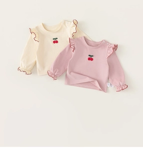 Detail of baby cotton shirts featuring cherry embroidery and ruffled lace sleeves