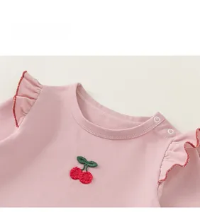 Close-up of pink cotton baby top with shoulder ruffles and red cherry embroidery detail