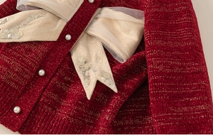 Dettaglio del cardigan in maglia rossa con fiocchi dorati, paillettes e bottoni a perla