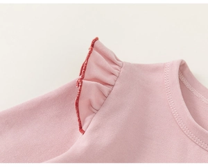 Detail of pink cotton girl's top featuring ruffle shoulders and red lockstitch seams