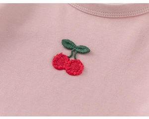 Close-up of pink knit fabric with a detailed red cherry embroidery and ribbed texture