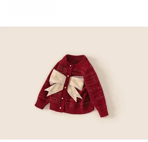 Dettaglio del cardigan rosso da bambina con grande fiocco dorato e bottoni di perle