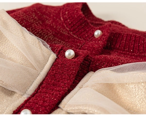 Dettaglio di cardigan in maglia rossa con filo dorato, bottoni di perle e bordo in tulle