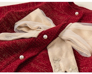 Dettaglio macro del cardigan rosso per bambina con fiocco dorato e bottoni in perle