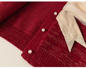 Dettaglio del cardigan festivo rosso con bottoni di perle e fiocco dorato brillante