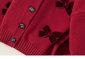 Dettaglio del cardigan in maglia rosso scuro con fiocchi di velluto e bottoni retrò