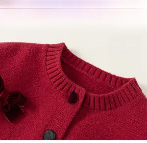 Dettaglio del cardigan in maglia rossa con fiocco in velluto e bottoni dorati con fiocchi