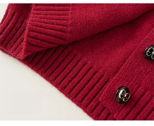 Dettaglio del cardigan in maglia rossa con bordo a coste e bottoni con fiocco argento