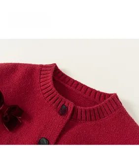 Dettaglio del cardigan rosso in maglia con fiocchi di velluto e bottoni dorati