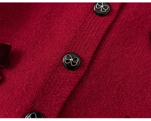 Dettaglio del cardigan in maglia rosso scuro con bottoni neri e decorazioni a fiocco oro