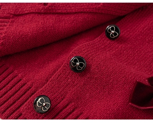 Dettaglio ravvicinato del cardigan rosso in maglia con bottoni neri e fiocco in velluto