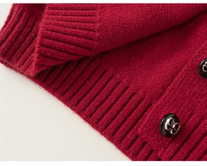 Dettaglio del cardigan in maglia rossa con bottoni neri e oro con fiocco in rilievo